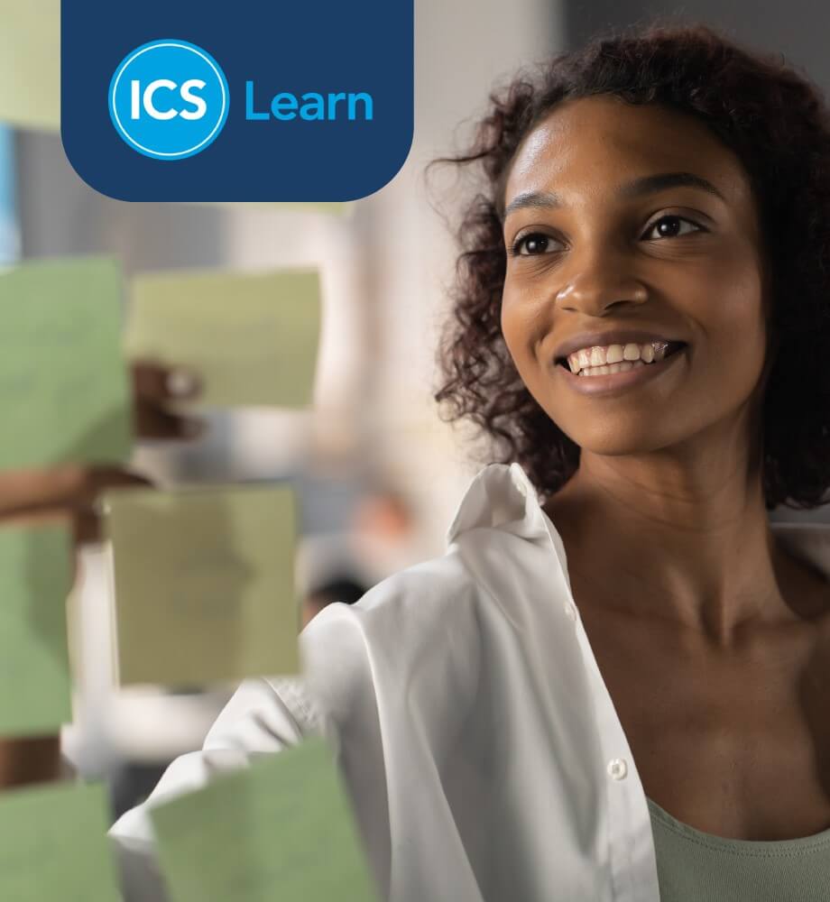 Smiling woman organizing sticky notes in a modern office, representing ICS Learn’s eLearning approach to project management.